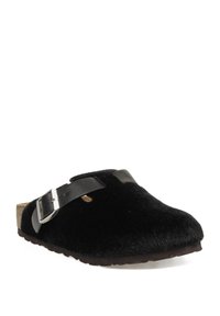 Zueco negro sin cordones con parte superior de pelo, correa de cuero ajustable con hebilla plateada y suela marrón texturizada.