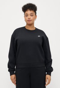 Sweatshirt noir court avec des manches longues, des poignets côtelés et un petit logo brodé sur la poitrine. Texture douce, design décontracté.