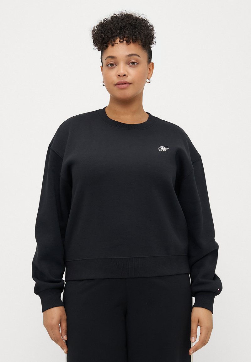 Sweatshirt noir court avec des manches longues, des poignets côtelés et un petit logo brodé sur la poitrine. Texture douce, design décontracté.