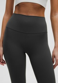 Korkeavyötäröiset, tummanharmaat legginsit, jotka on valmistettu sileästä ja joustavasta materiaalista. Ominaisuuksiin kuuluu saumatonta muotoilua, jossa on hienovaraisia ompelutietoja.