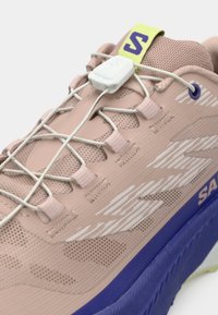 Αθλητικό παπούτσι ανοιχτό ροζ με ανώτερο μέρος από δίχτυ, λευκές λεπτομέρειες, ελαστικά κορδόνια και μπλε σόλα. Διαθέτει πράσινο ταμπελάκι στη φτέρνα με λογότυπο.