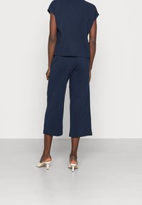 Navy blue cotton top with short sleeves, paired with navy wide-leg pants. The model wears light-colored heeled mules.