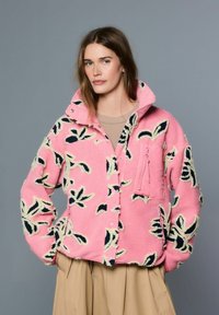 Roza flis jakna z rožnim vzorcem v mornarsko modri in krem barvi, z žepom na prsih z zadrgo in visokim ovratnikom.