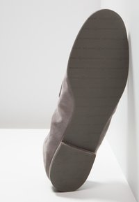 Semelle d'une botte en daim gris inclinée vers le haut, affichant la marque "Kennel & Schmenger" imprimée sur la semelle en caoutchouc foncé et le talon.