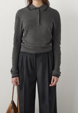 Femme portant un pull polo cintré à manches longues en maille côtelée gris foncé et un pantalon large taille haute couleur charbon, tenant un sac à main marron.