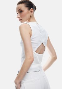 Witte mouwloze top met ribbeltextuur en een uitsnijding aan de achterkant, met een aansluitende silhouet. Gestyled met witte onderkleding.