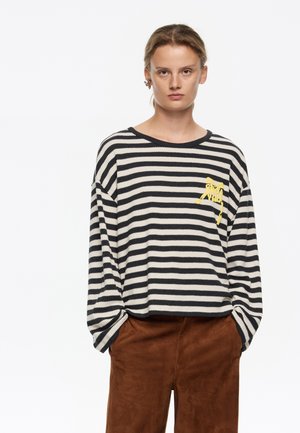 Pasiasty sweter w kolorze kremowym i czarnym, z żółtą grafiką na klatce piersiowej. Luźny krój z okrągłym dekoltem i miękką teksturą.