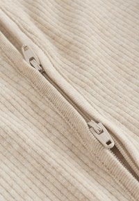 Zbliżenie beżowej prążkowanej tkaniny z częściowo rozpiętym pasującym beżowym zamkiem błyskawicznym.