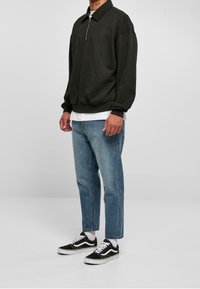 Svart zip-up sweatshirt med krage, kombinerad med ljusblå tapered jeans och svarta Vans sneakers. Mjuk material, avslappnad passform och subtil textur.