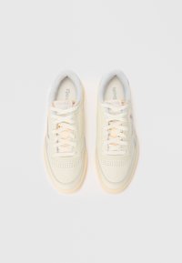 Kreemivärvi tossud perforatsiooni ehk augudega varbakaitse, valged paelad, heledat halli aktsenti ja kummist tallad. Omab Reebok'i logo keeles.