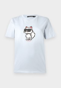 Světle modré bavlněné tričko s potiskem karikaturní kočky nosící sluneční brýle. Design je odvážný s černými konturami a červenými akcenty.