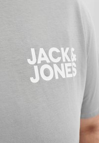 Close-up of a light gray T-shirt with white "JACK & JONES" text printed on the chest.