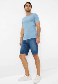 Lyseblå T-shirt med rund hals, parret med denimshorts i knælængde. Båret med hvide sneakers. Glat stof, afslappet pasform, minimal detaljer.