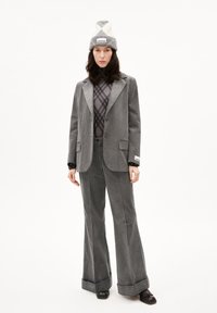 Grijze corduroy pak met wijde broekspijpen en een getailleerde blazer. Gelaagd met een geruit topje en afgewerkt met een twee-kleurige gebreide muts.