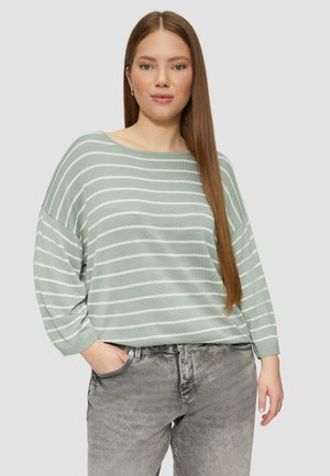 Jasnozielony sweter w paski o luźnym kroju i szerokim dekolcie, w połączeniu z szarymi dżinsami. Sweter ma długie rękawy i miękką fakturę.