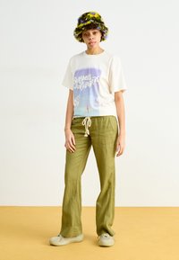 Cream t-shirt with a pastel graphic design, paired with olive green linen pants. Accessorized with a multicolored fuzzy bucket hat.