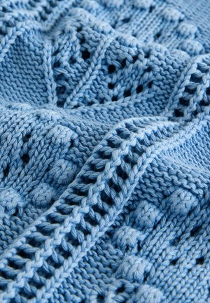 Světle modrý pletený textil s texturovaným vzorem obsahujícím vystouplé prvky, copánky a krajkový detail. Hladký povrch, měkký materiál.