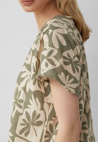 Bluse mit Blumenmuster in Creme und Olivgrün. Leichter, strukturierter Stoff mit kurzen Ärmeln und einer lockeren Passform.