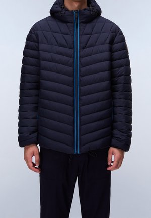 Homme portant une doudoune matelassée bleu marine avec capuche et fermeture éclair bleu vif, debout les bras détendus le long du corps.