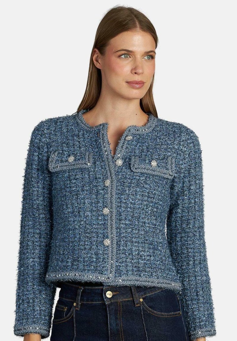 Giacca in tweed blu con due taschini sul petto, chiusura con bottoni metallici e design accorciato. Presenta una finitura texturizzata e un collo rotondo.