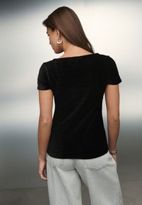 Sort velour top med korte ærmer, tekstureret mønster, rund halsudskæring og figursyet design. Kombineret med lysegrå jeans med vide ben.