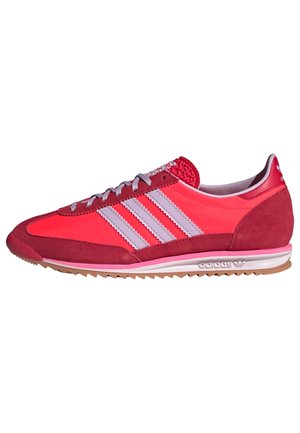 Low-top Adidas sneaker i rød med pink og hvide striber, snørelukning foran og tekstureret gummisål vist fra siden.