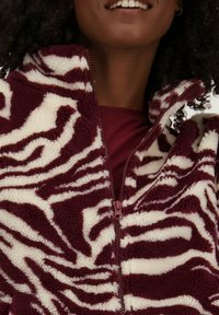 Bordeaux en crèmekleurige fleecejack met een zebra-patroon, volledige rits met hoge kraag en zachte, gestructureerde stof.