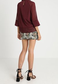 Bordeaux blouse met een doorschijnende overlay en een keyhole achterkant, gecombineerd met een mini-rokje met bloemenprint. Zwarte blockhakken sandalen met banden.