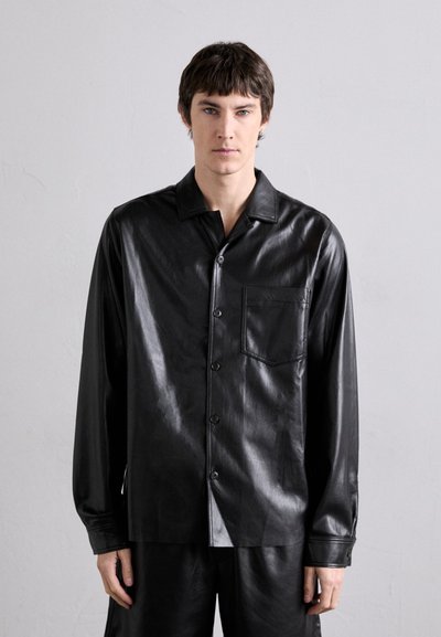 Camisa de cuero negro abotonada con un bolsillo en el pecho, de mangas largas y una textura suave, combinada con pantalones a juego.