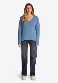 Lichtblauwe gebreide trui met een V-hals, losse pasvorm en lange mouwen, gecombineerd met donkere denim jeans en lichtgekleurde sneakers.