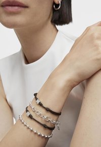 Tres pulseras en una muñeca: una es de cuero marrón con acentos de plata, otra es una cadena de plata y la última cuenta con cuentas de plata.