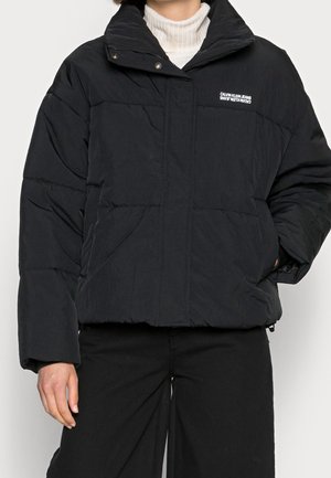 Doudoune noire avec un col montant, boutons-pression et design matelassé. Présente un logo sur la poitrine gauche et une coupe décontractée.