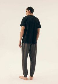 Black short-sleeve t-shirt and gray relaxed-fit pants with cuffed hems. The fabric appears soft with a subtle texture. Model stands barefoot.