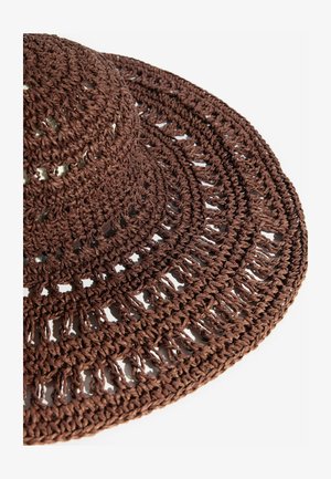 Pruun laia äärega punutud õledest müts avatud töö mustri ja tekstuurse punutisega, kujutatud valgel taustal.
