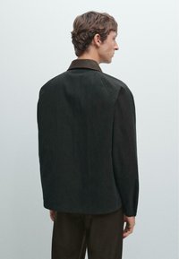 Black, lightweight shirt with a structured design, collared neckline, and long sleeves. Features a smooth texture and slight drape.