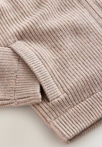 Suéter de punto acanalado color beige claro con tela texturizada, que presenta un puño doblado y sutiles variaciones de color a lo largo de toda la prenda.