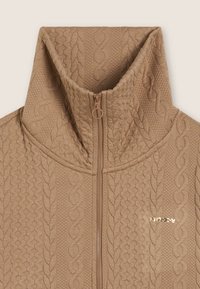 Sweat à fermeture éclair en tricot beige avec col montant et motif en maille torsadée, doté d'une tirette de fermeture éclair circulaire et d'un petit logo doré sur la poitrine.