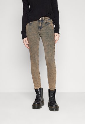 Jeans ajustados marrones deslavados con un acabado texturizado, presentando un cierre de botón y cremallera. Combinados con botas de combate negras con cordones.