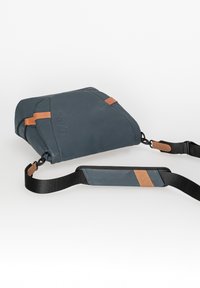 Dark blue bag with a textured finish, featuring brown leather accents and a wide, adjustable strap. Zipper closure visible.