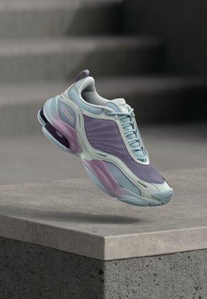 Jasnoniebieski i fioletowy sportowy but z grubą podeszwą unoszący się nad szarym betonowym parapetem w miękkim naturalnym świetle.