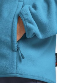 Giacca in fleece blu con tasca con zip, tessuto testurizzato e rifiniture a contrasto sui polsini e sull'orlo. Etichetta con logo visibile di lato.