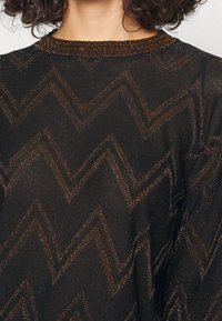 Svart tröja med ett zigzag-mönster i metallisk koppartråd, med en strukturerad stickad finish och en ribbad halsringning.