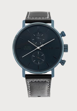 Montre-bracelet noire Hugo avec bracelet en cuir, deux sous-cadrans affichant le jour et la date, aiguilles argentées et index horaires minimalistes sur un cadran sombre.