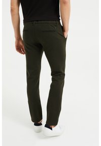 Green textured trousers with a slim fit, featuring back pockets and a black button accent. Paired with white shoes and a black shirt.