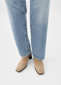 Beige suede ankle boots with a pointed toe and low black block heel, worn with light blue straight-leg jeans.