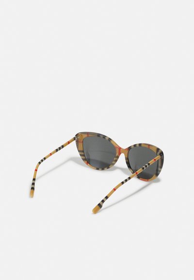 Lunettes de soleil en œil de chat avec des verres gris, présentant une monture beige et noire à motifs avec des accents rouges et des embouts de branches rayés.