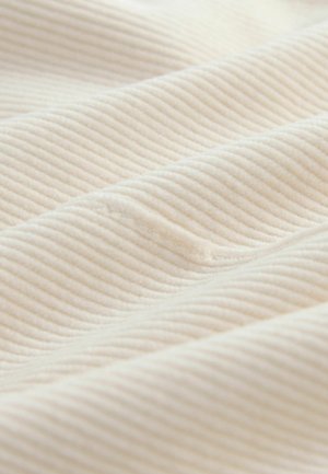 Texturovaná tkanina ve světlé krémové barvě se zvýrazněným diagonálním žebrováním. Materiál vypadá jemně a nadýchaně, zvýrazňuje hloubku a jemný lesk.