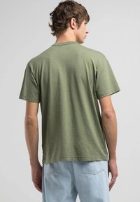 Camiseta de color verde oliva, de manga corta, hecha de algodón suave, con cuello redondo y un corte relajado. Tela ligera con una textura sutil.