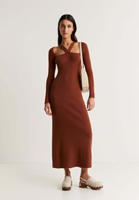 Rostfarbendes, geripptes Strickkleid mit langen Ärmeln, tiefem Ausschnitt und Ausschnittdetails. Kombiniert mit Plateauschuhen mit gewellten Kanten.