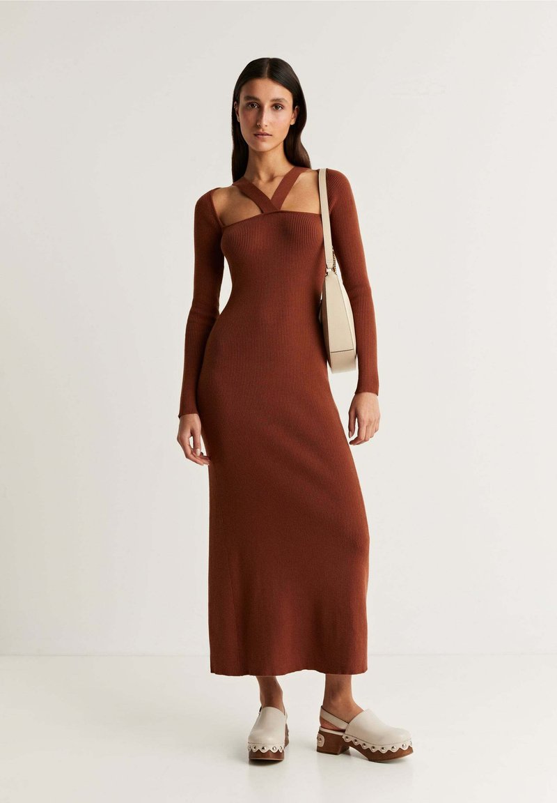 Rostfarbendes, geripptes Strickkleid mit langen Ärmeln, tiefem Ausschnitt und Ausschnittdetails. Kombiniert mit Plateauschuhen mit gewellten Kanten.